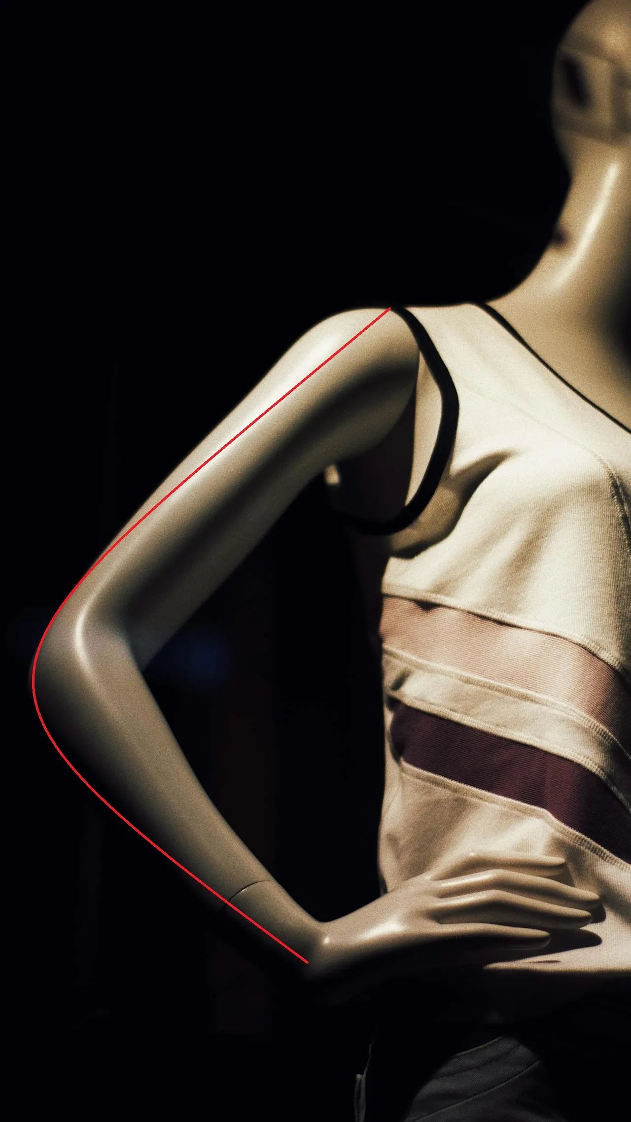 Maniquí indicando con una línea roja curva cómo medir el largo de manga desde el hombro hasta la muñeca.